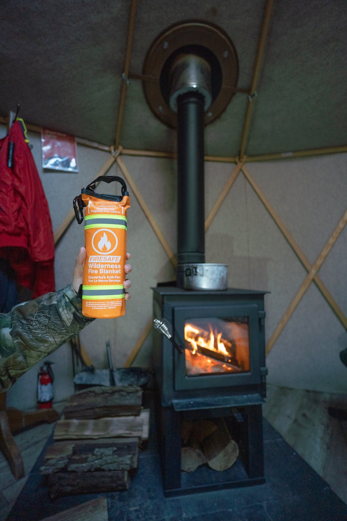 Person holding a FireSafe fire blanket pouch inside a yurt with a wood stove and fire extinguisher nearby