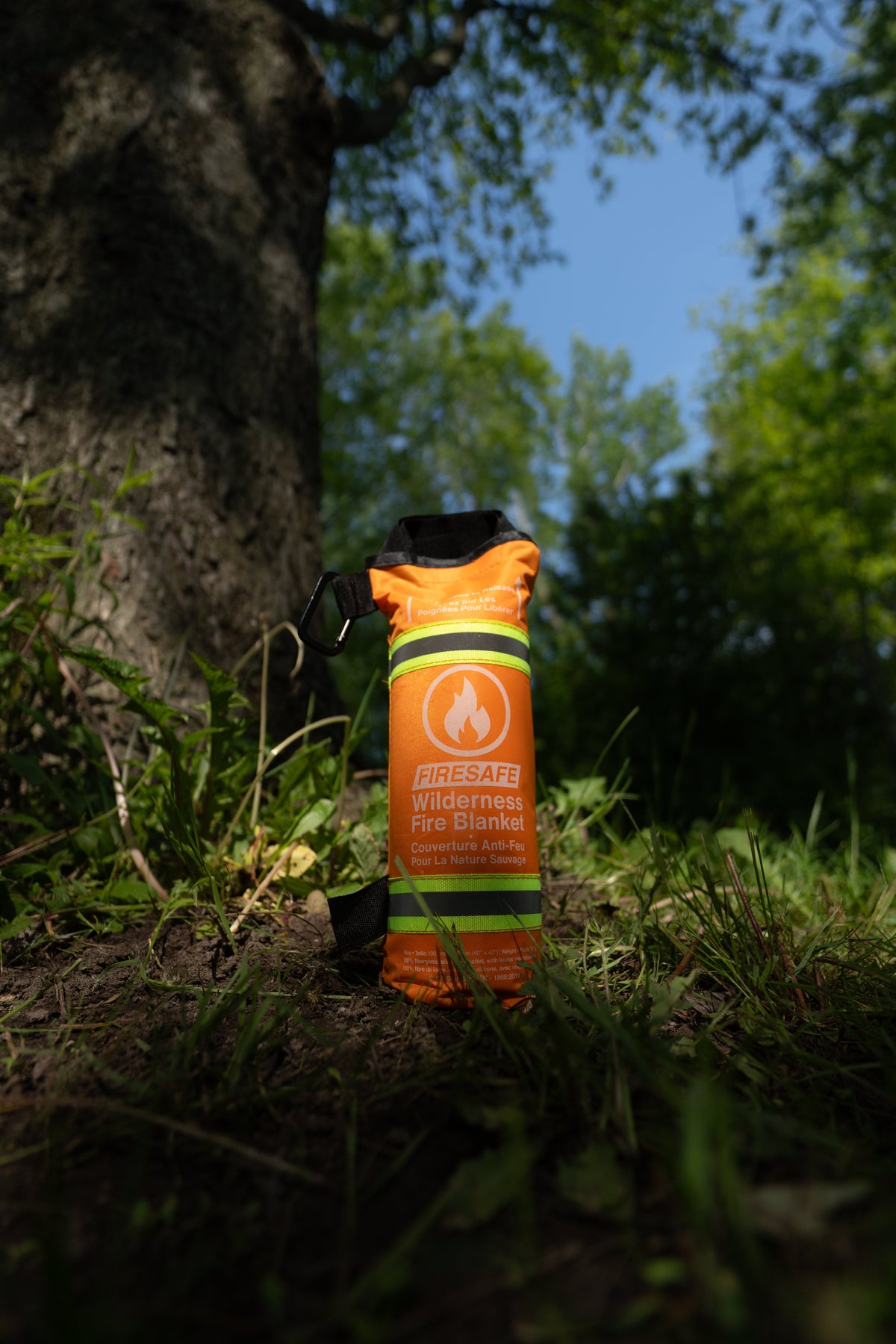 FireSafe Wilderness Fire Blanket standing at the base of a tree trunk outdoors with blue sky and forest backdrop