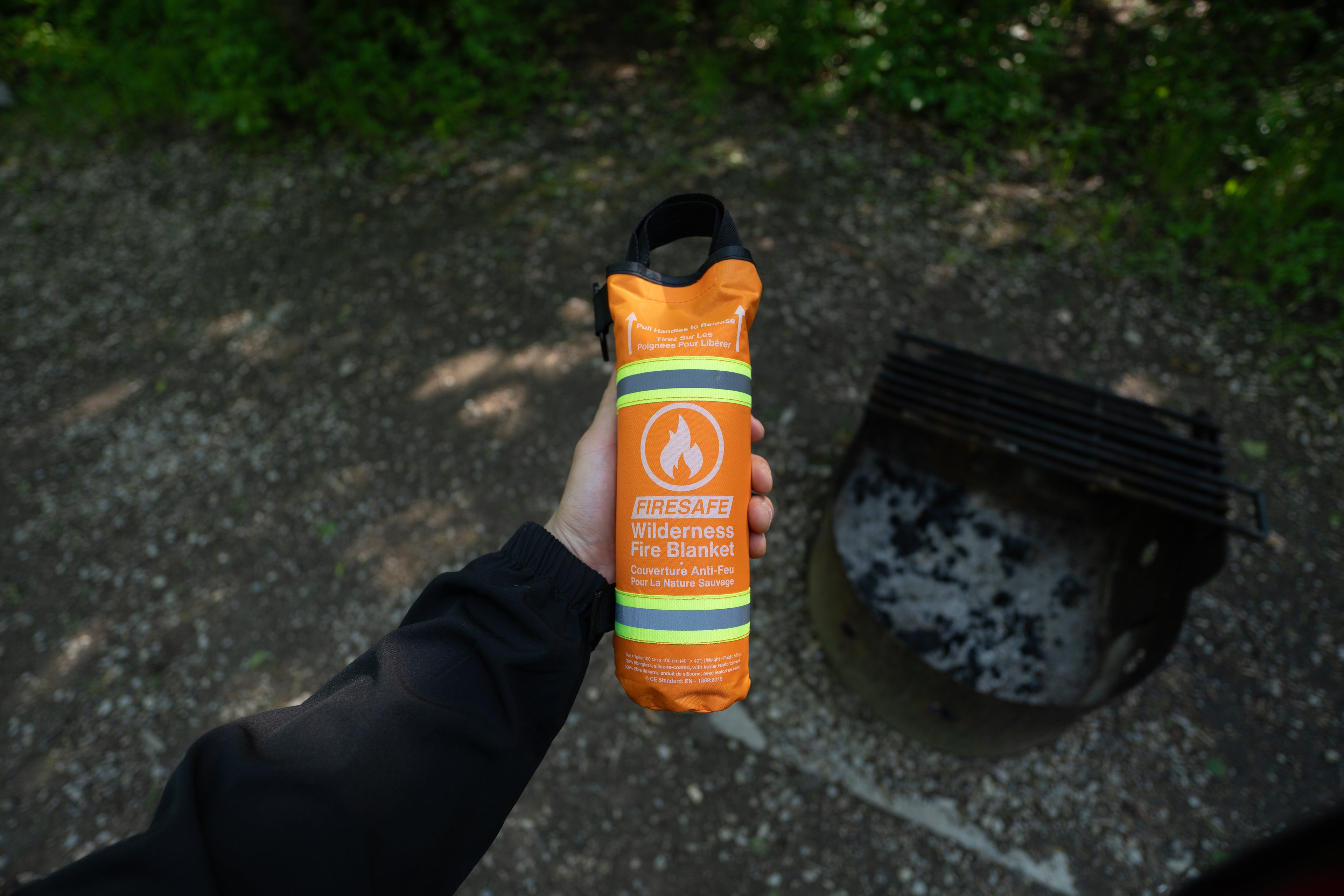First-person view holding the FireSafe near a campfire ring in the forest