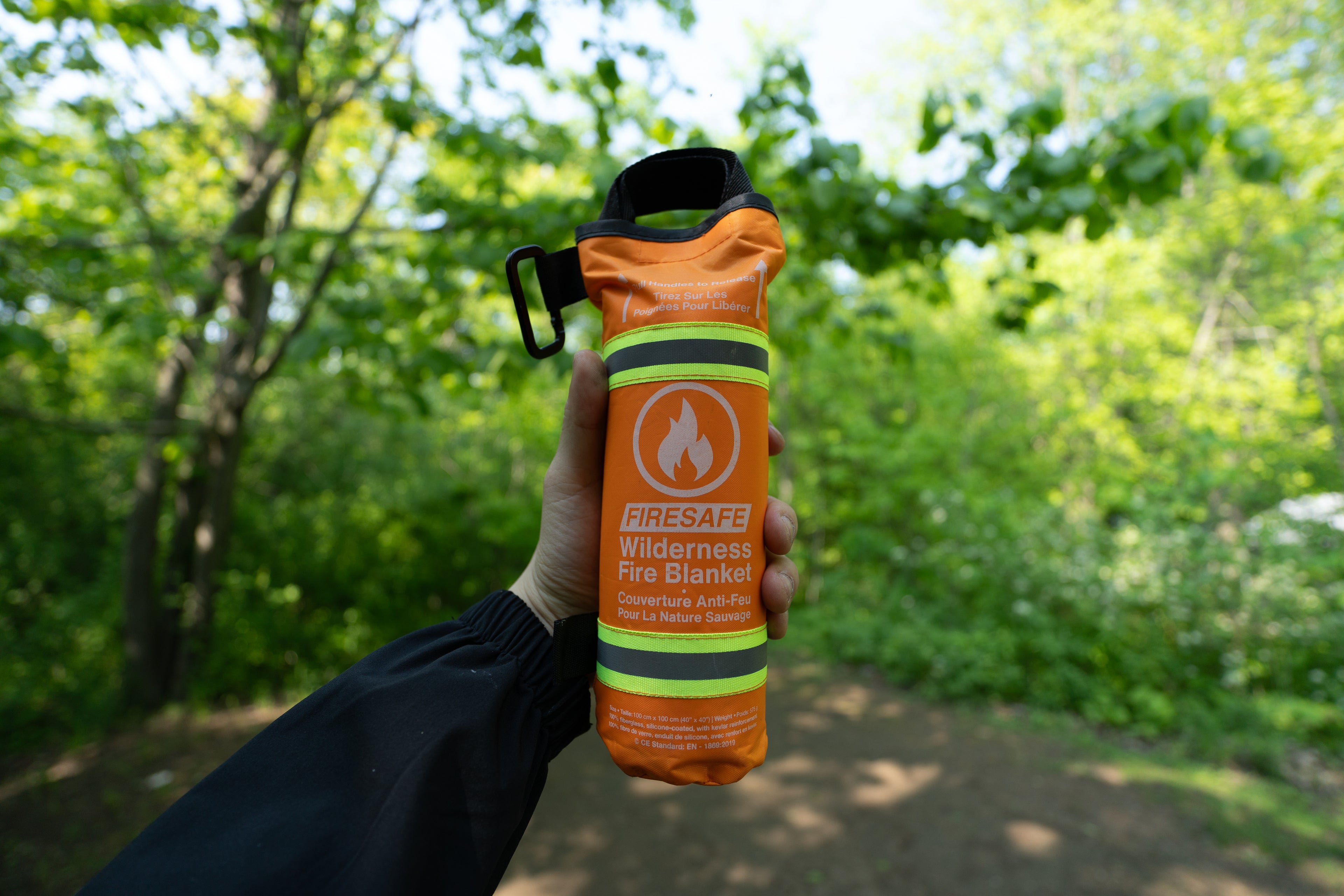 First-person view holding the FireSafe Wilderness Fire Blanket in a forest clearing