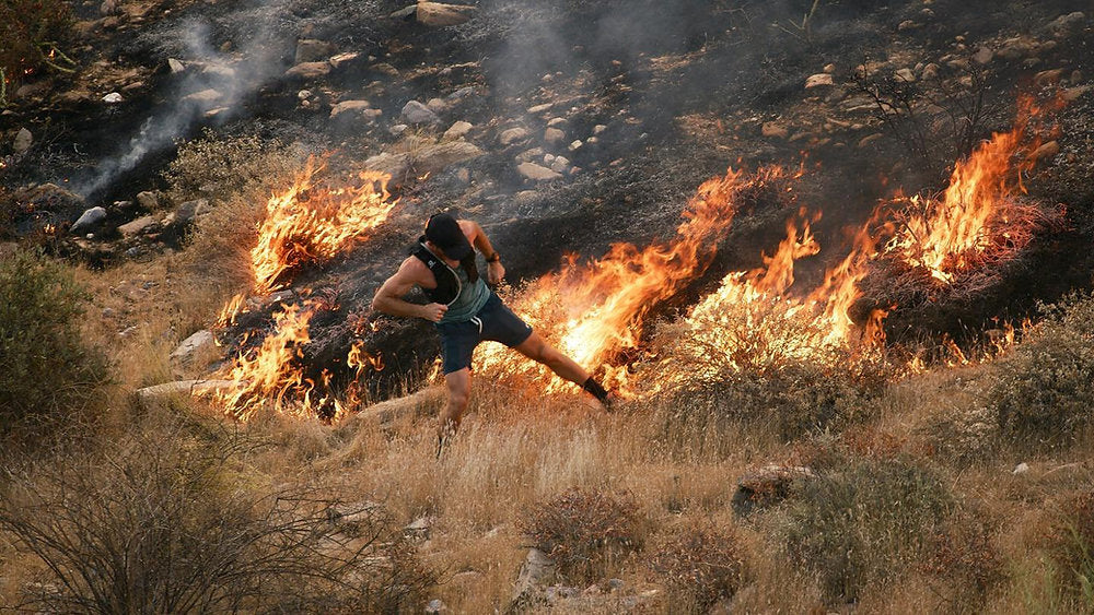 Person running across a hillside adjacent to an active brush fire